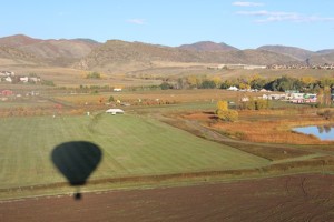 Figure 3 Airborne, ascending & looking west at our shadow. The Denver Botanical Gardens at Chatfield corn maze and pumpkin patch are off in the distance in the middle of the picture