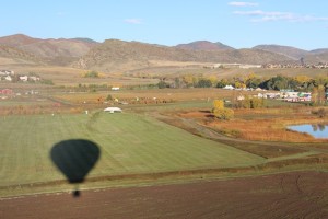 Figure 3 Airborne, ascending & looking west at our shadow. The Denver Botanical Gardens at Chatfield corn maze and Pumpkin patch are off in the distance in the middle of the picture